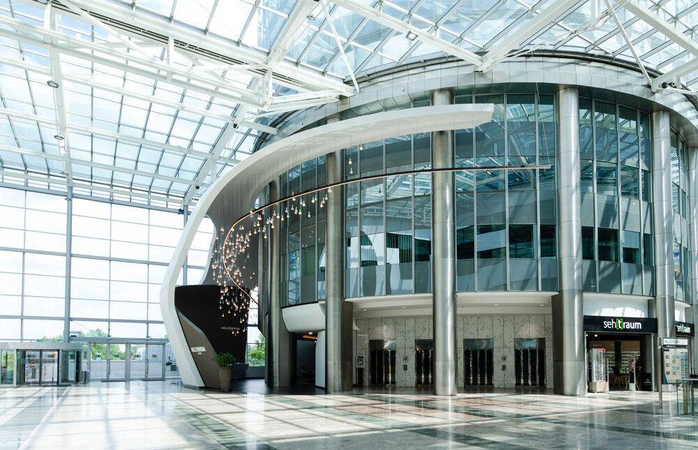 Geräumige, moderne Lobby mit beeindruckender Glasdachkonstruktion und geschwungenen Designelementen.