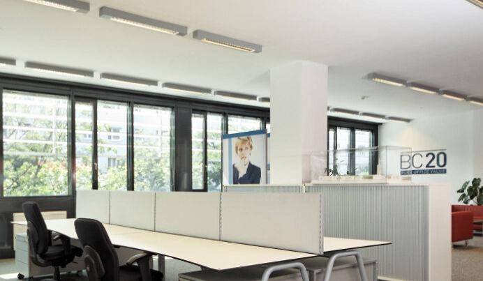 Heller Großraumbüro mit mehreren Arbeitsplätzen, Trennwänden und großen Fenstern mit Blick ins Grüne.