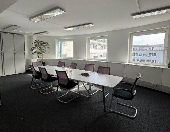 Konferenzraum mit einem langen Tisch, modernen Stühlen und Fenstern, die einen Blick auf umliegende Gebäude ermöglichen.