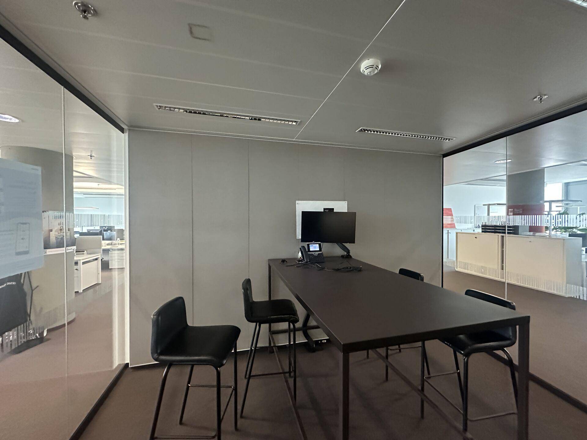 Moderner Besprechungsraum mit hohem Tisch und Stühlen, umgeben von Glaswänden, ideal für Teamarbeit.
