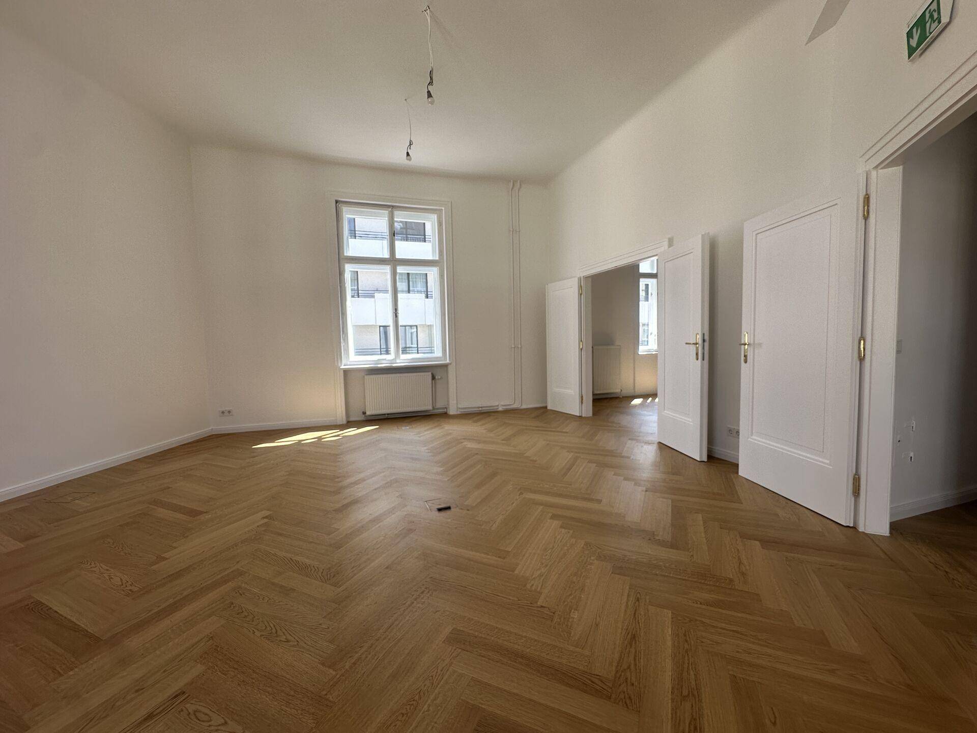 Großer, heller Raum mit Fischgrätparkett und hohen Fenstern, ideal für Büronutzung oder Veranstaltungen.