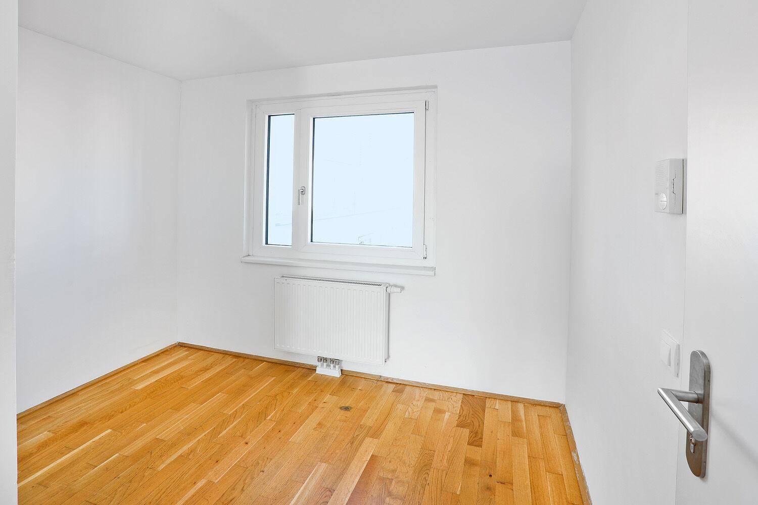 Freundliches Schlafzimmer mit Parkettboden und einem großen Fenster für optimale Belichtung.