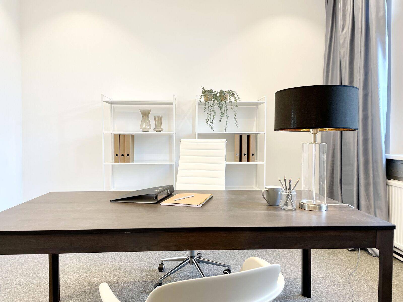 Detailansicht eines modernen Büros mit Schreibtisch, Lampe, weißen Regalen und Büromaterialien.