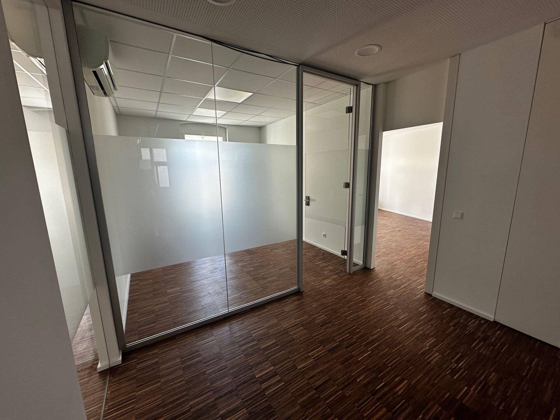 Büro mit Holzboden und moderner Glastrennwand, die den Raum in separate Bereiche gliedert.