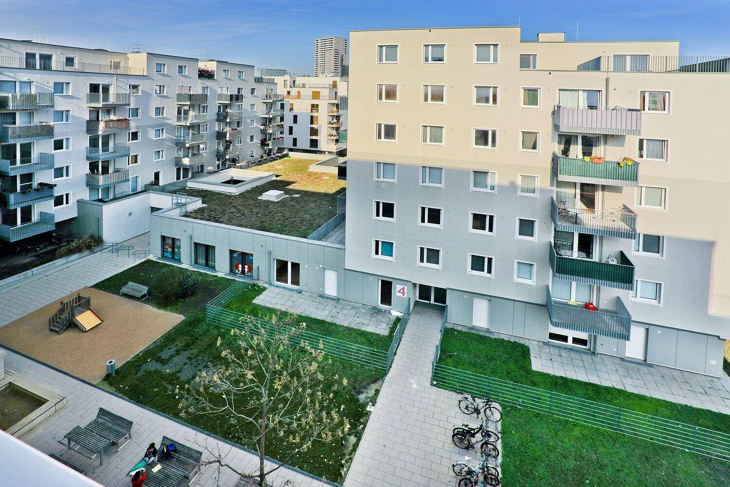 Vogelperspektive auf einen Innenhof mit Spielplatz, Rasenflächen und Fahrradabstellplätzen.