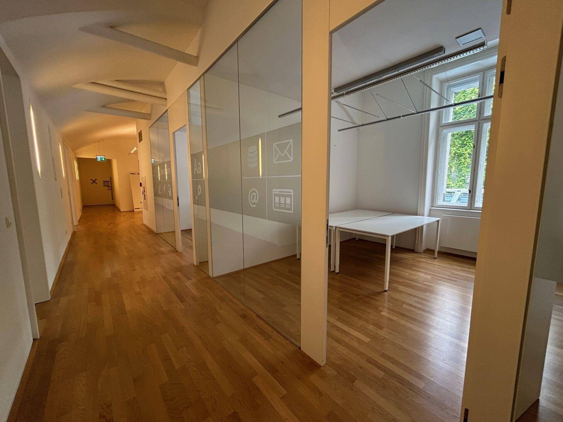 Moderner Bürogang mit Glaswänden zu den Büros und durchgehendem Fischgrätparkettboden.