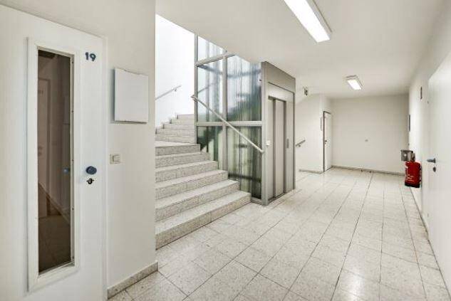 Heller Treppenaufgang mit modernem Glasaufzug und gefliestem Boden in einem Mehrfamilienhaus.
