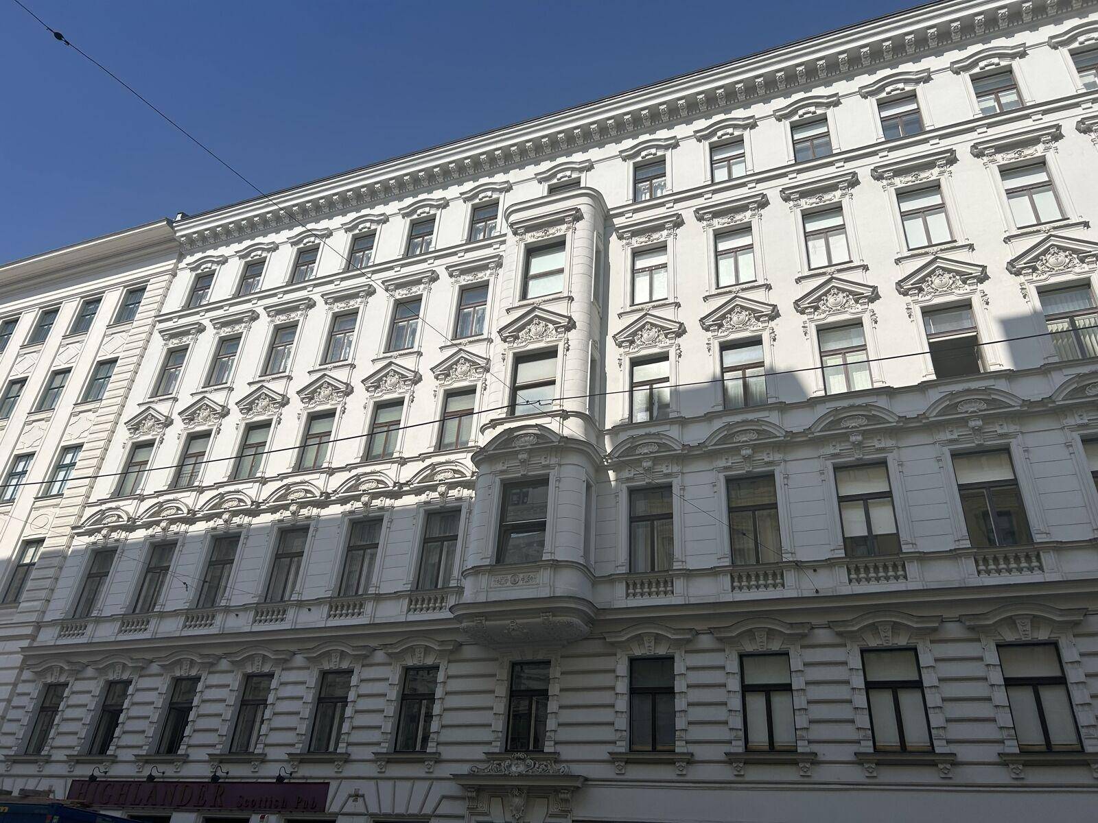 Eine weitere Ansicht der eleganten weißen Gebäudefassade mit detaillierten Verzierungen und zahlreichen Fenstern im Sonnenlicht.