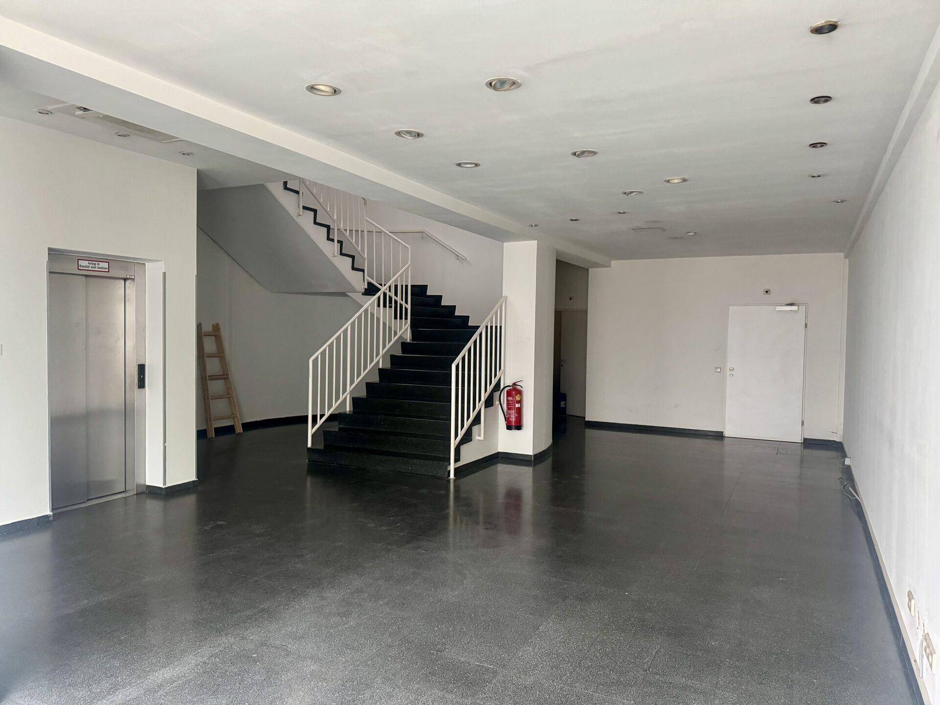 Geräumiger Eingangsbereich mit dunklem Boden, einer Treppe und einem Aufzug.