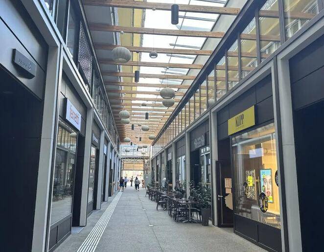 Überdachte Einkaufspassage mit Geschäften, Cafés und einer Glasdachkonstruktion, die für helle Atmosphäre sorgt.