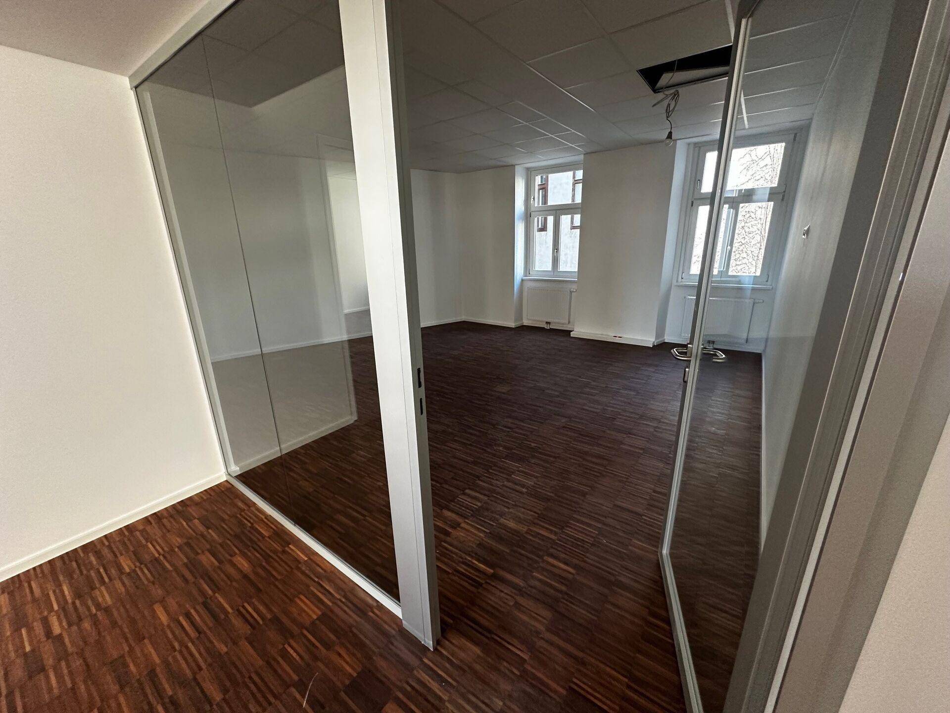 Büro mit Holzboden und moderner Glastrennwand, die den Raum in Bereiche unterteilt.