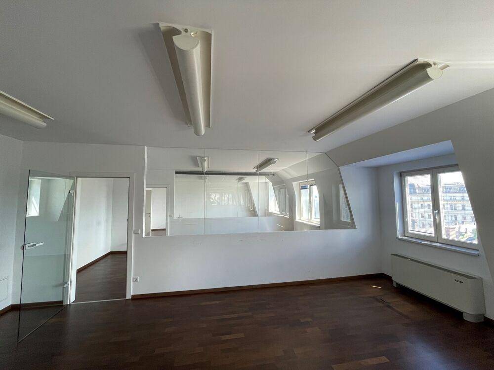 Geräumiger Büroraum mit Holzboden, Glaswand und Fenstern, die Tageslicht hereinlassen.