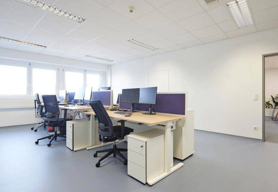 Großraumbüro mit mehreren Arbeitsplätzen, ergonomischen Stühlen und hellgrauem Bodenbelag.