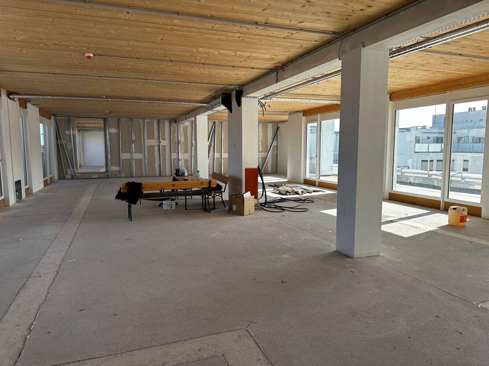 Großer, offener Raum im Rohbau mit Holzbalkendecke und Betonboden, bereit für den Innenausbau.