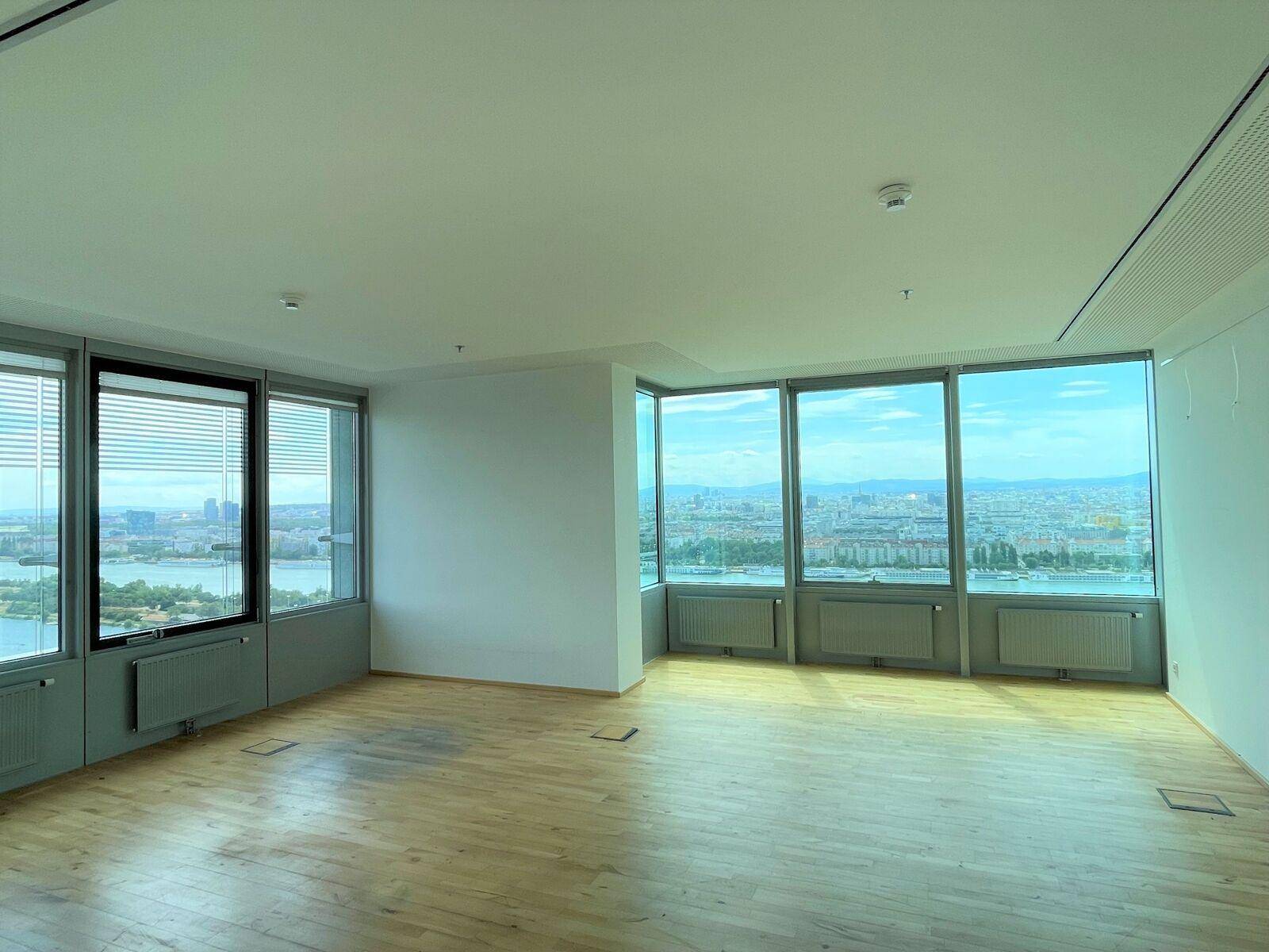 Heller Büroraum mit Panoramablick auf die Stadt und den Fluss, ausgestattet mit Heizkörpern unter den großen Fenstern.