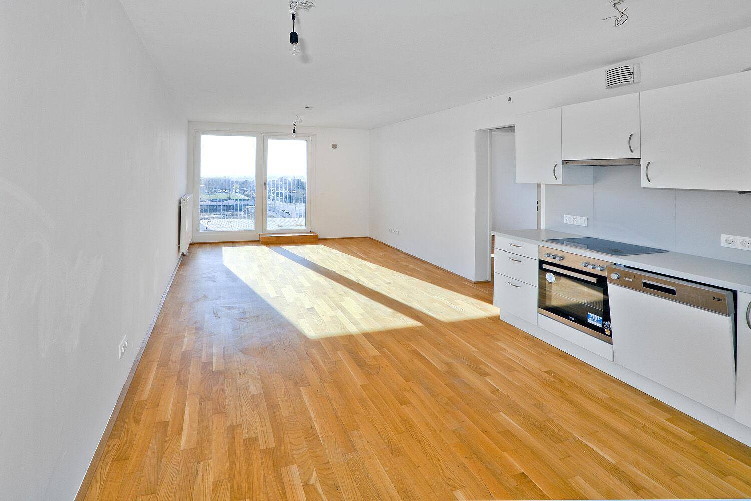 Offener Wohnbereich mit integrierter Küche, Parkettboden und viel Tageslicht.