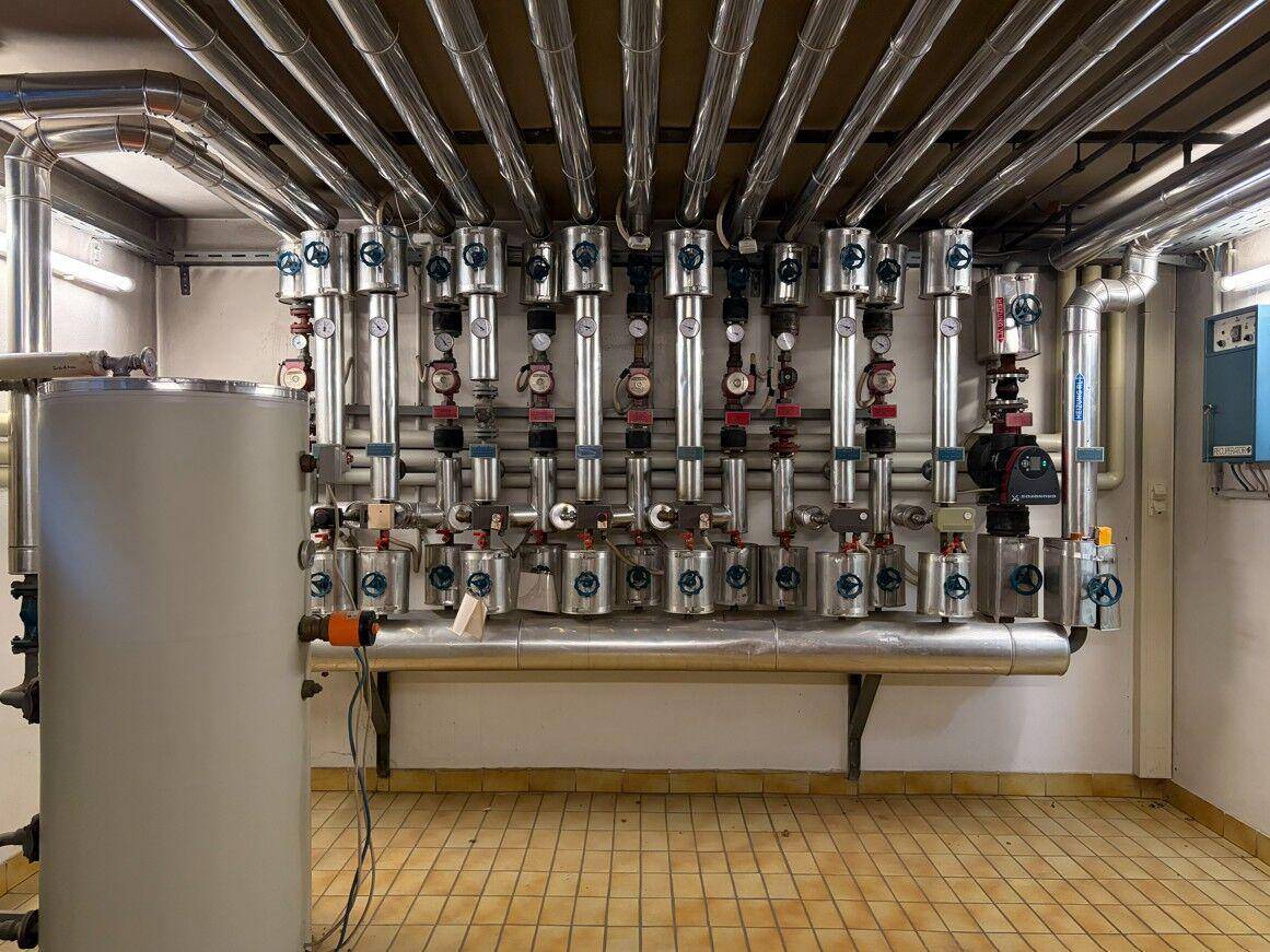 Technikraum mit komplexen Rohrleitungen, Ventilen und einem großen Warmwasserspeicher.