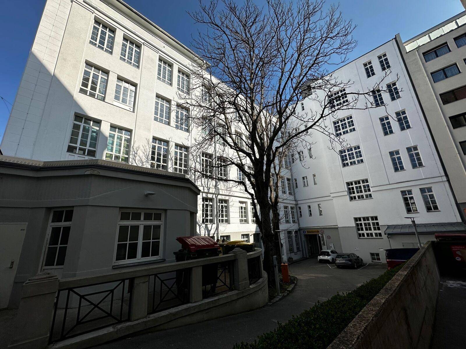 Innenhofansicht eines Gebäudes mit weißer Fassade und vielen Fenstern, umgeben von Bäumen.