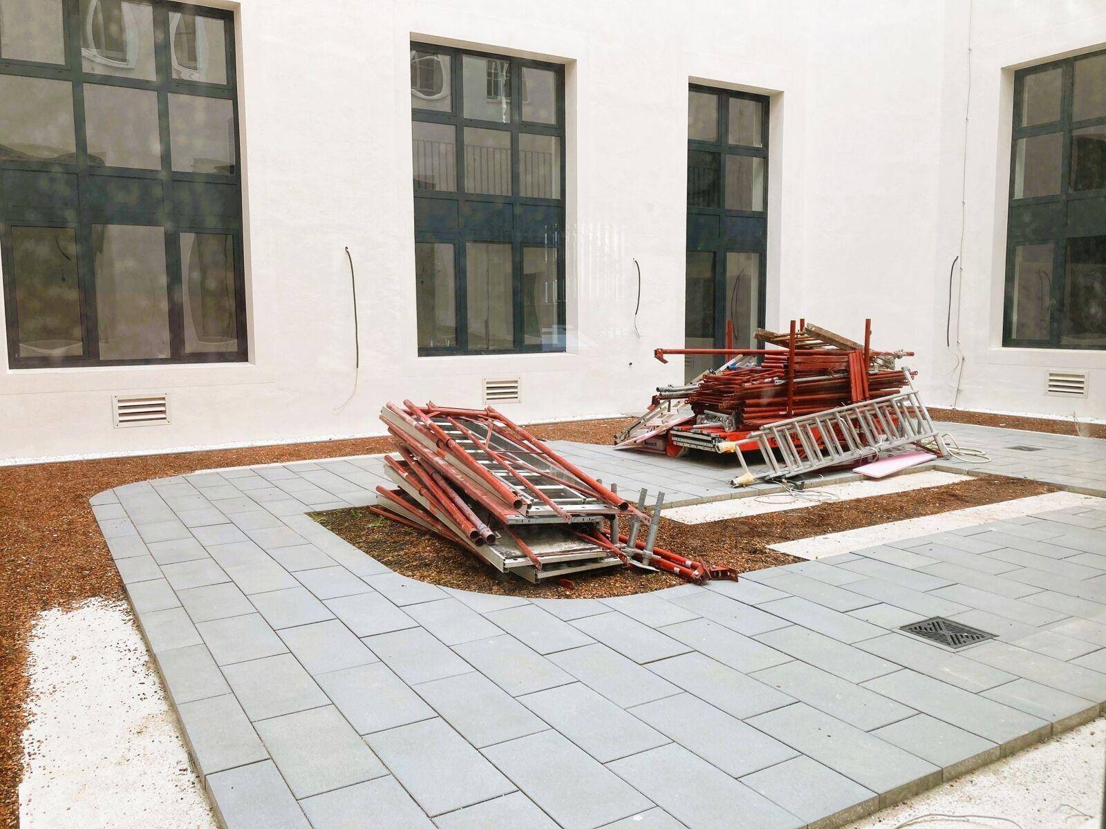 Innenhof im Bau mit neuen Pflastersteinen, Kiesflächen und Baumaterialien, umgeben von Gebäudefassaden.