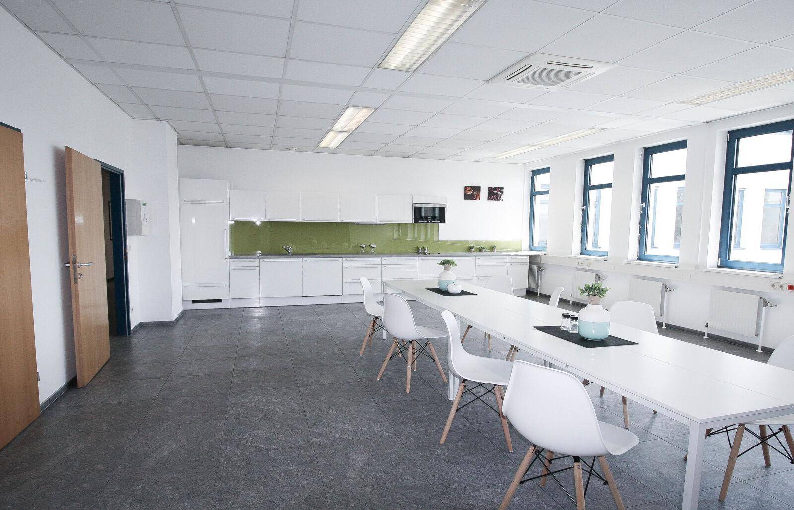 Geräumige moderne Küche mit Essbereich, weißen Schränken, großen Fenstern und integrierten Geräten.