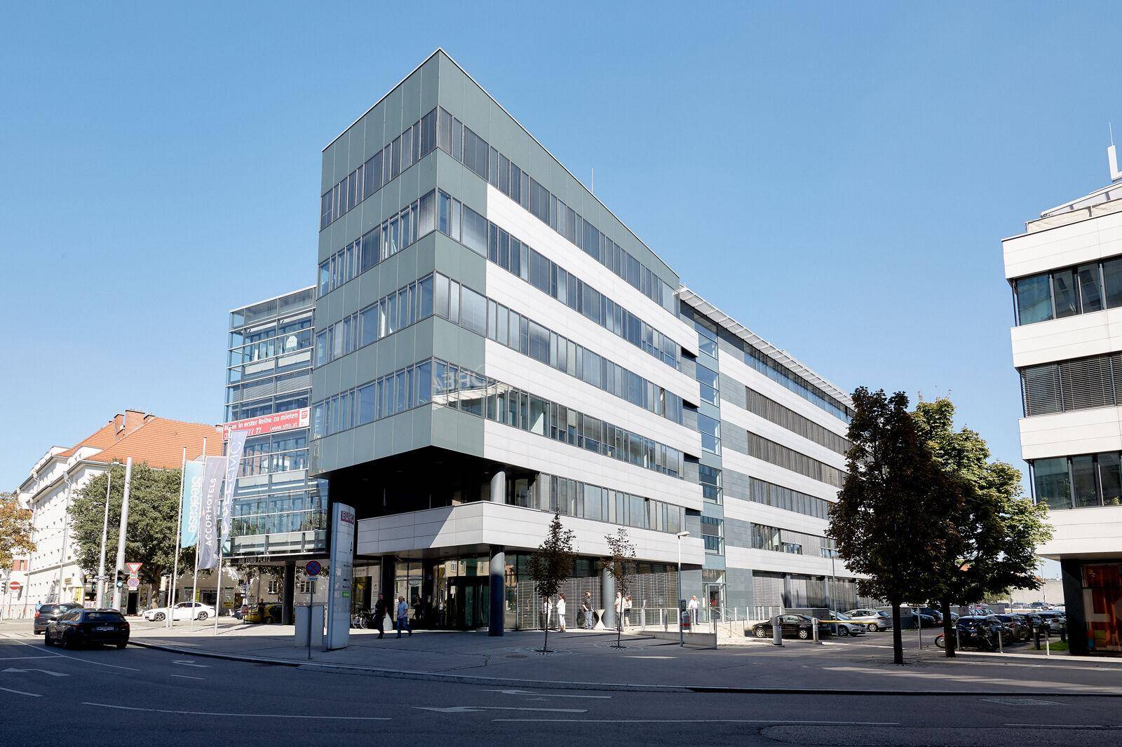 Modernes Bürogebäude mit markanter Architektur an einer belebten Straße mit parkenden Autos.