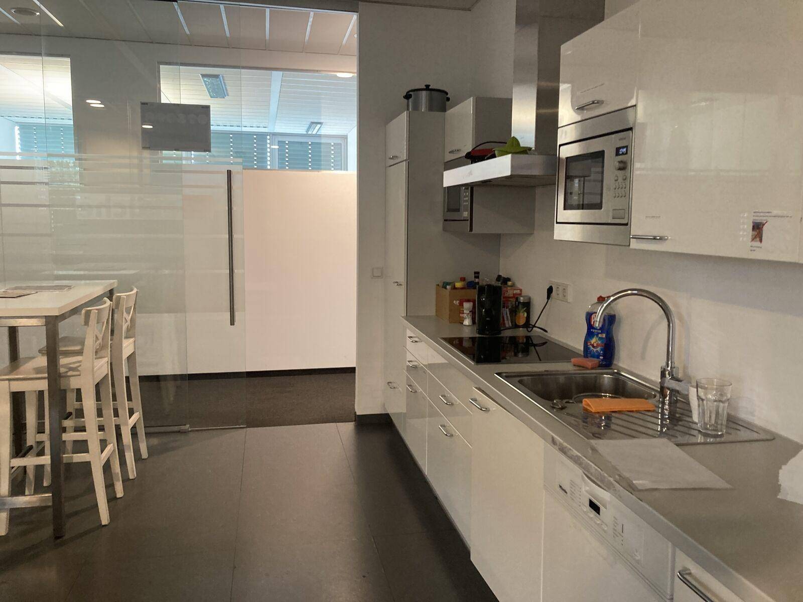 Moderne Küche mit weißen Hochglanzschränken, Edelstahlgeräten und einer Frühstückstheke mit Barhockern.