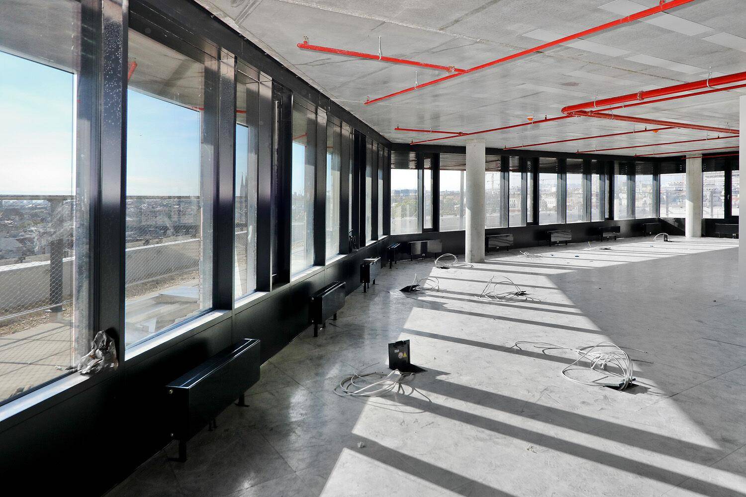 Heller Büroraum mit durchgehenden Fenstern und Betonboden, der viel Tageslicht hereinlässt und eine weite Aussicht über die Umgebung bietet.
