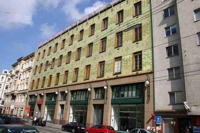 Seitenansicht des historischen Gebäudes mit markanter grüner Fassade und Geschäften im Erdgeschoss.