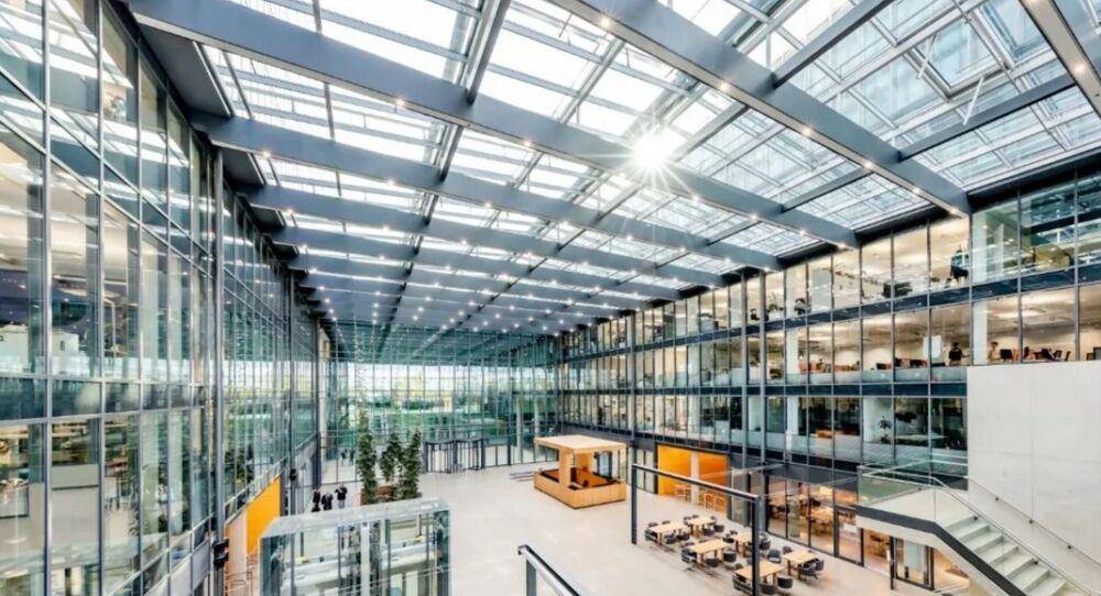 Großzügiges, lichtdurchflutetes Atrium mit Glasdach, modernen Sitzbereichen und offenen Büroflächen.