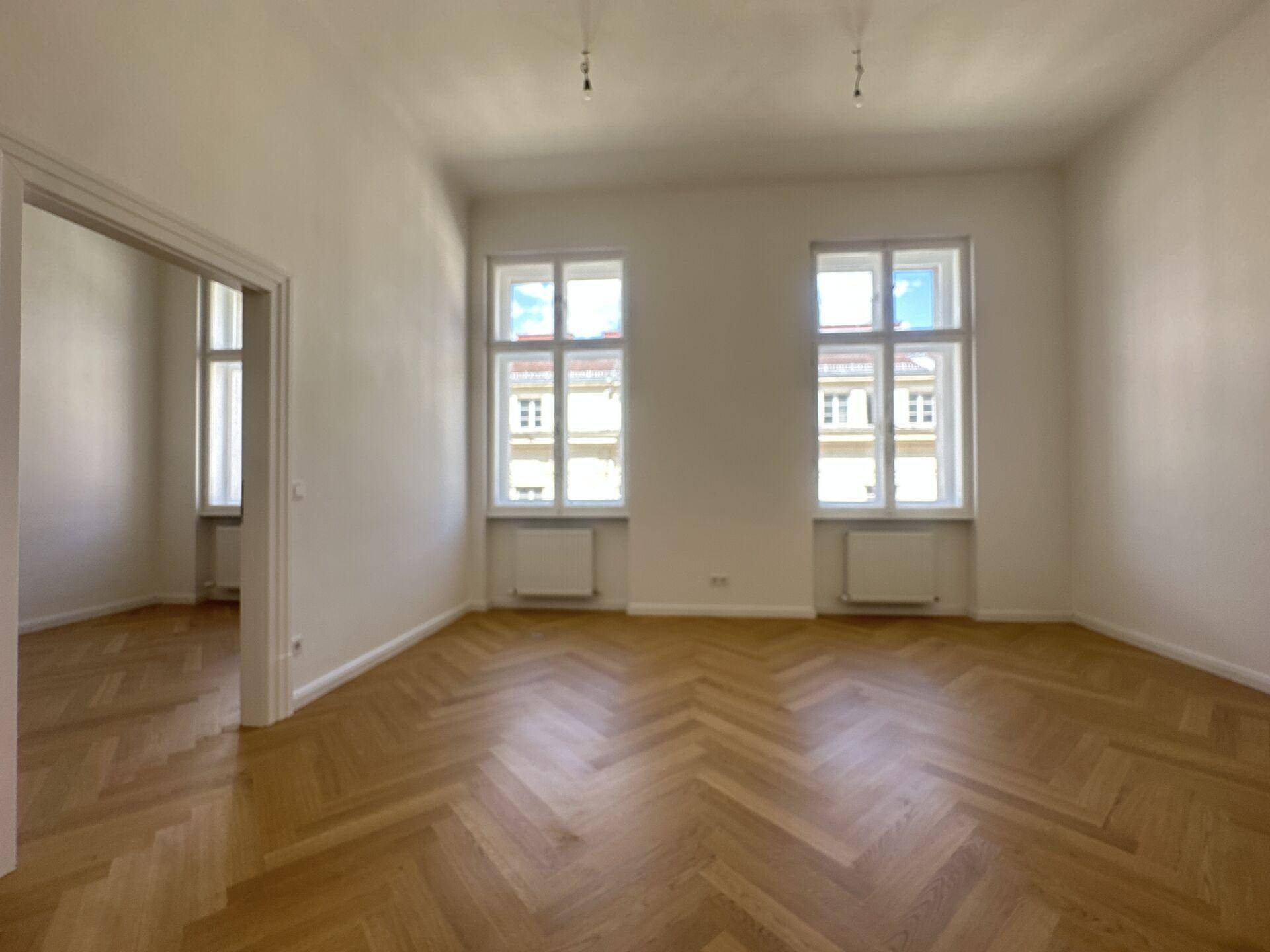 Heller Büroraum mit klassischem Fischgrätparkett und zwei großen Fenstern zur Straße.