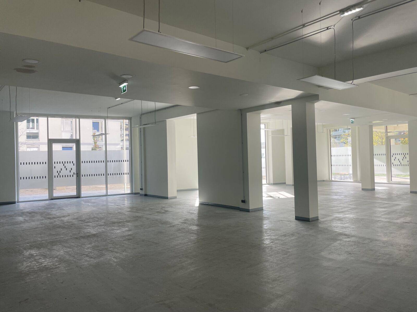 Weitläufiger, heller Gewerberaum mit Säulen und großen Fenstern, ideal für flexible Bürokonzepte.