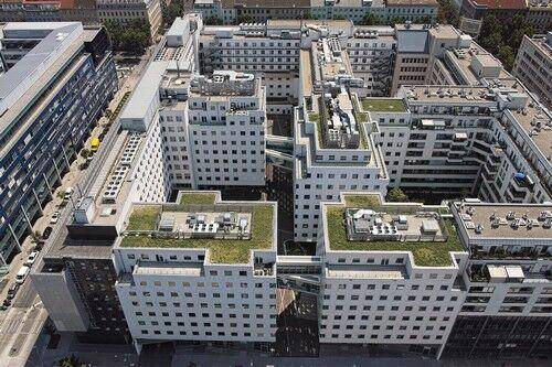 Luftaufnahme eines großen Gebäudekomplexes mit begrünten Dächern und Innenhöfen in städtischer Umgebung.
