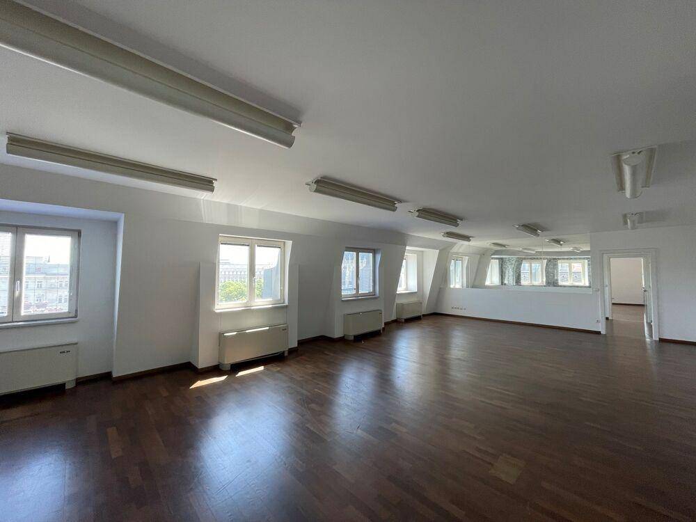 Geräumiger, leerer Raum mit Holzboden, vielen Fenstern und schrägen Decken im Dachgeschoss.