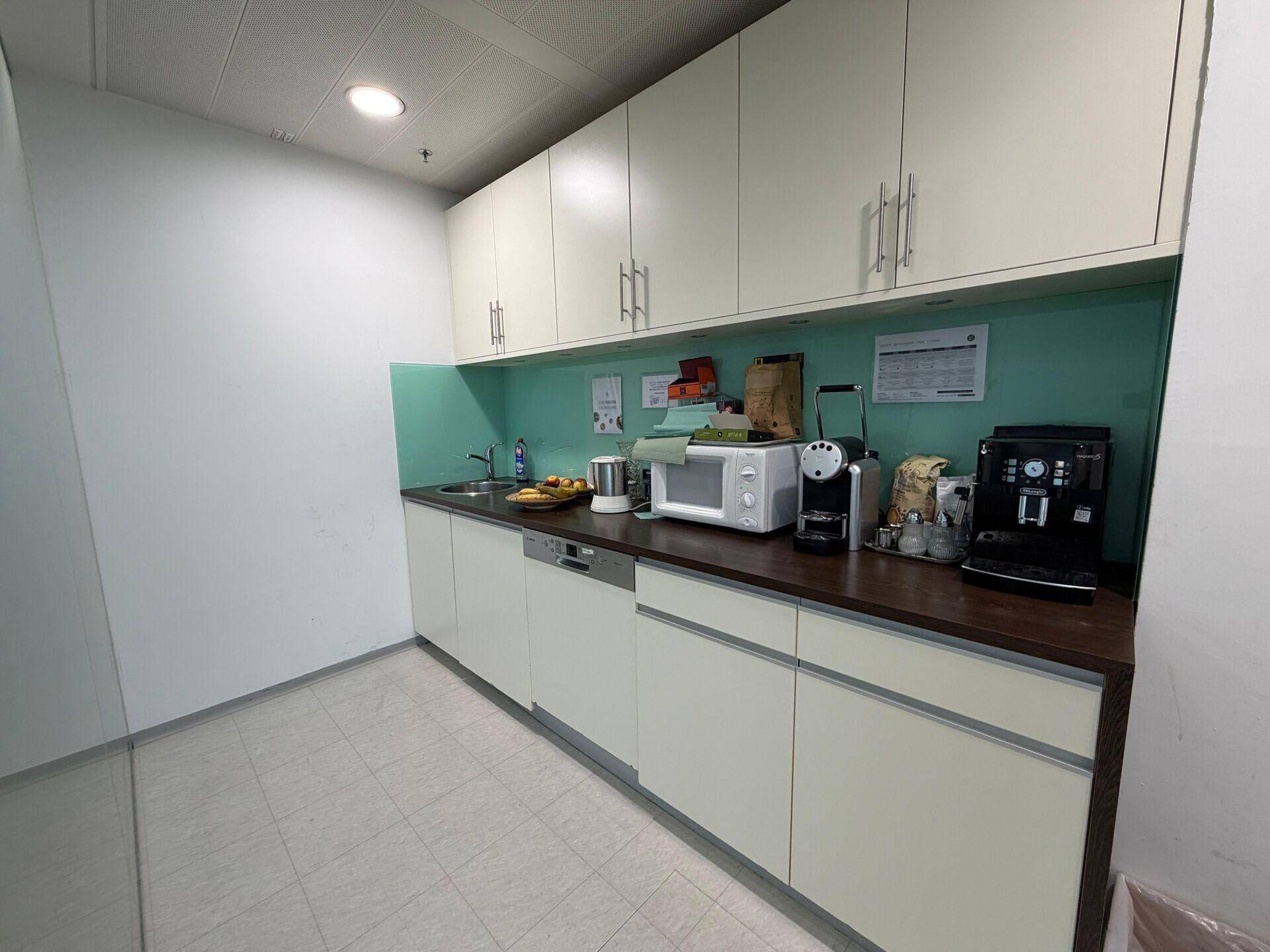 Funktionale Teeküche mit hellen Schränken, Spülmaschine, Mikrowelle und Kaffeemaschinen für den Büroalltag.