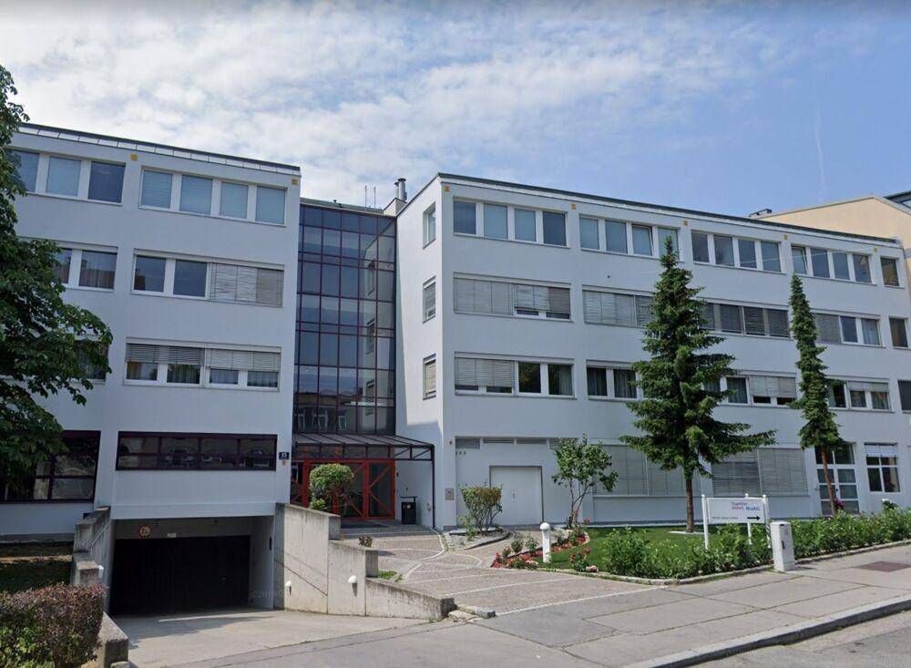 Modernes Bürogebäude mit Glasfassade, Zufahrt zur Tiefgarage und gepflegter Außenanlage.