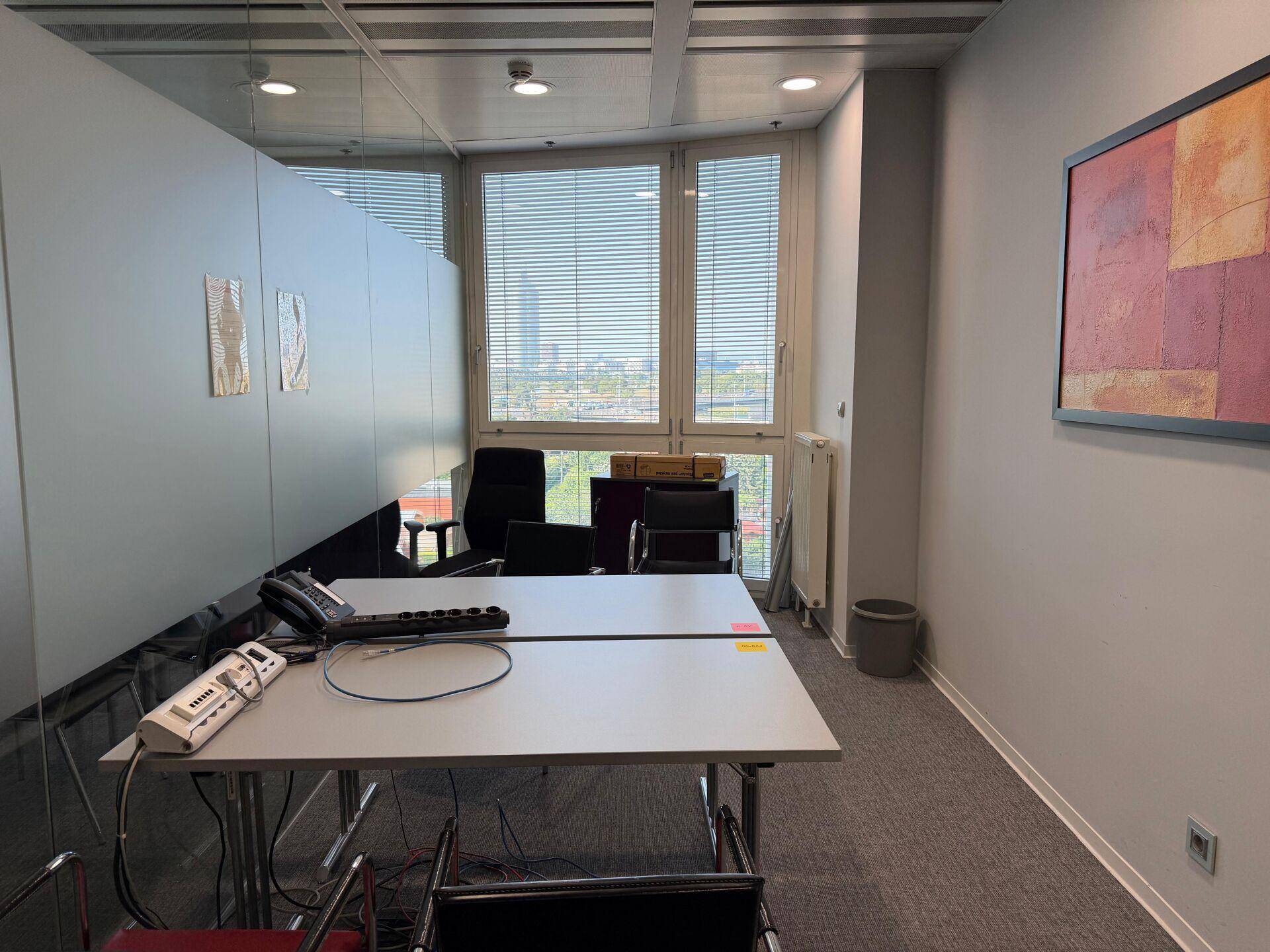 Büro mit zwei Schreibtischen, Fenster mit Jalousien und Blick auf die Stadt.