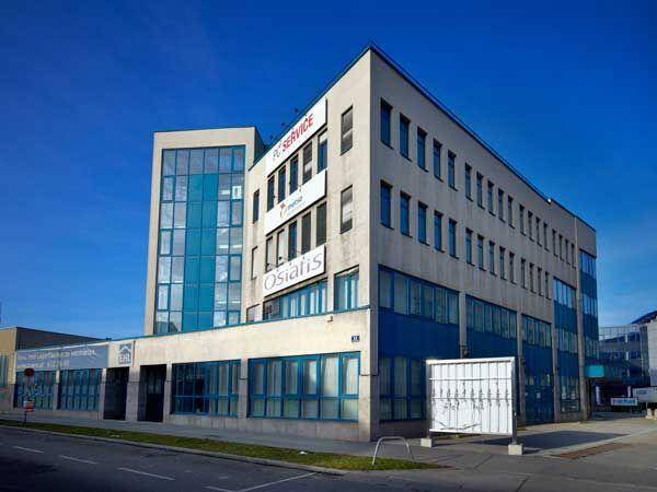 Ansicht des modernen Bürogebäudes von der Straße mit blauen Akzenten und großen Fenstern unter blauem Himmel.