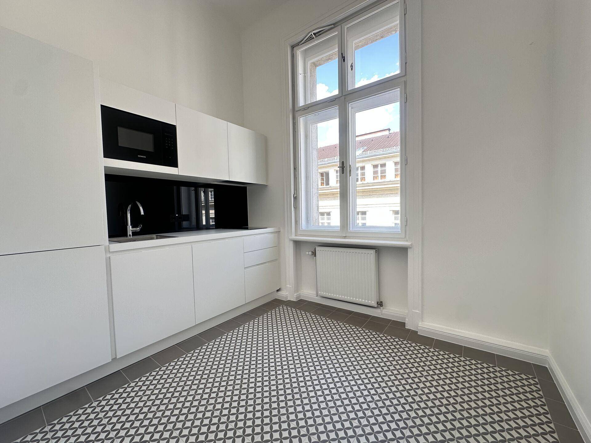 Moderne Küchenzeile mit weißen Schränken, integrierter Mikrowelle und gemustertem Fliesenboden.