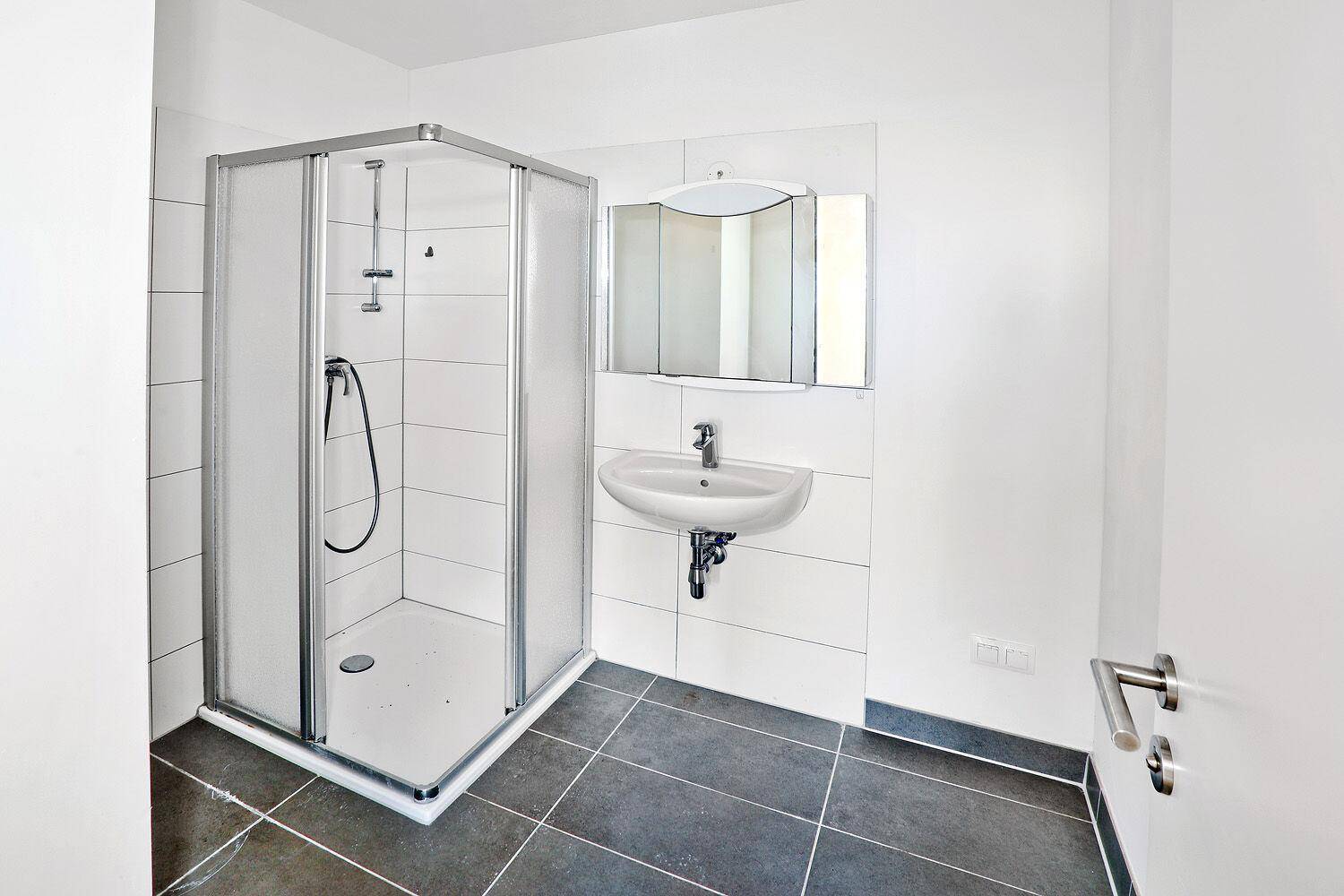 Modernes Badezimmer mit Duschkabine, Waschbecken und dunklen Bodenfliesen.