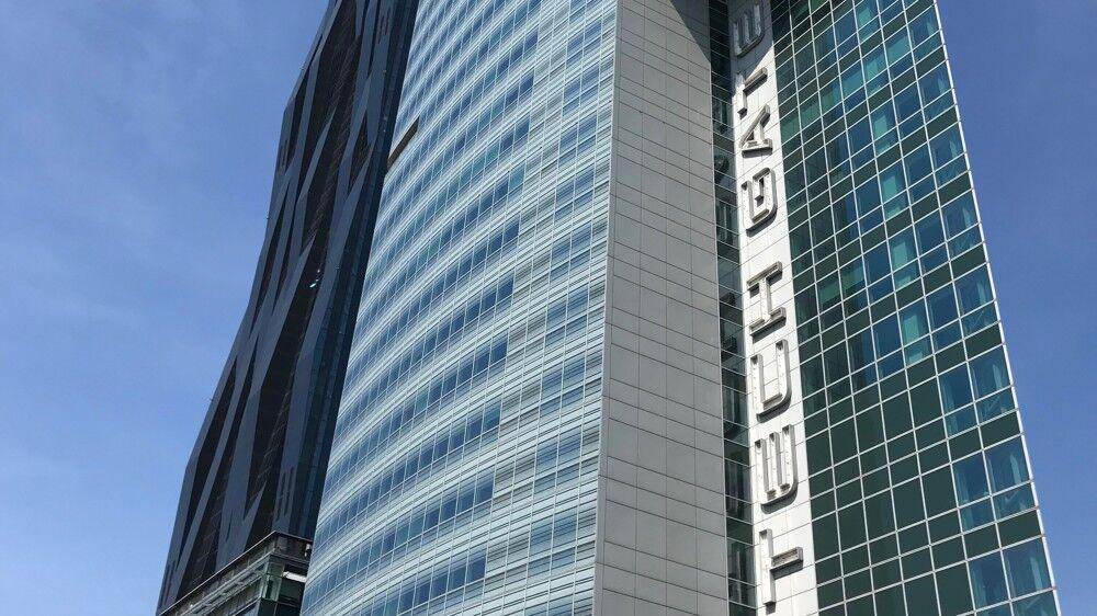 Detailansicht einer modernen Hochhausfassade mit Glas und vertikalen Schriftzügen unter blauem Himmel.