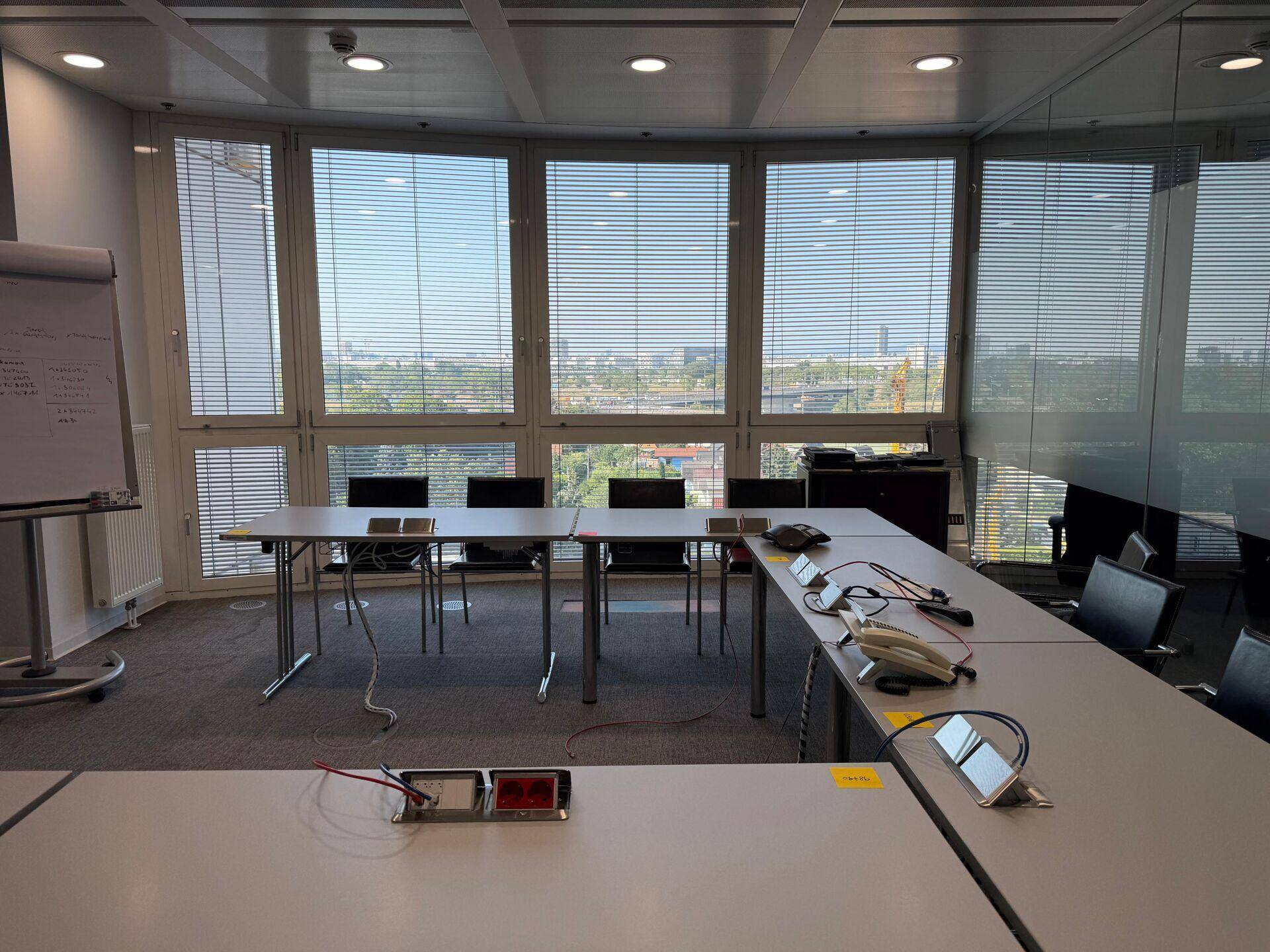 Großer Konferenzraum mit langen Tischen, vielen Stühlen und weitem Stadtblick.