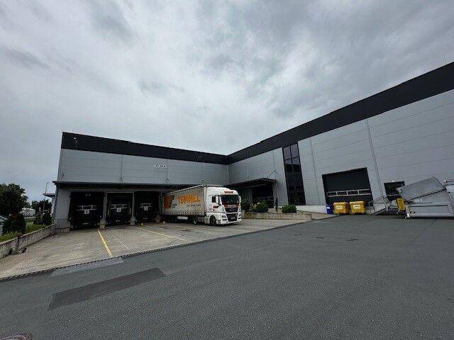 Moderne Industriefassade mit Laderampen und einem LKW, unter bewölktem Himmel.