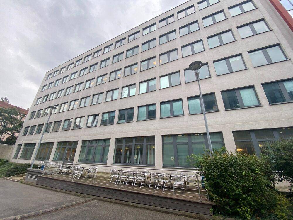 Modernes Bürogebäude mit vielen Fenstern und einer kleinen Außenterrasse im Erdgeschoss.