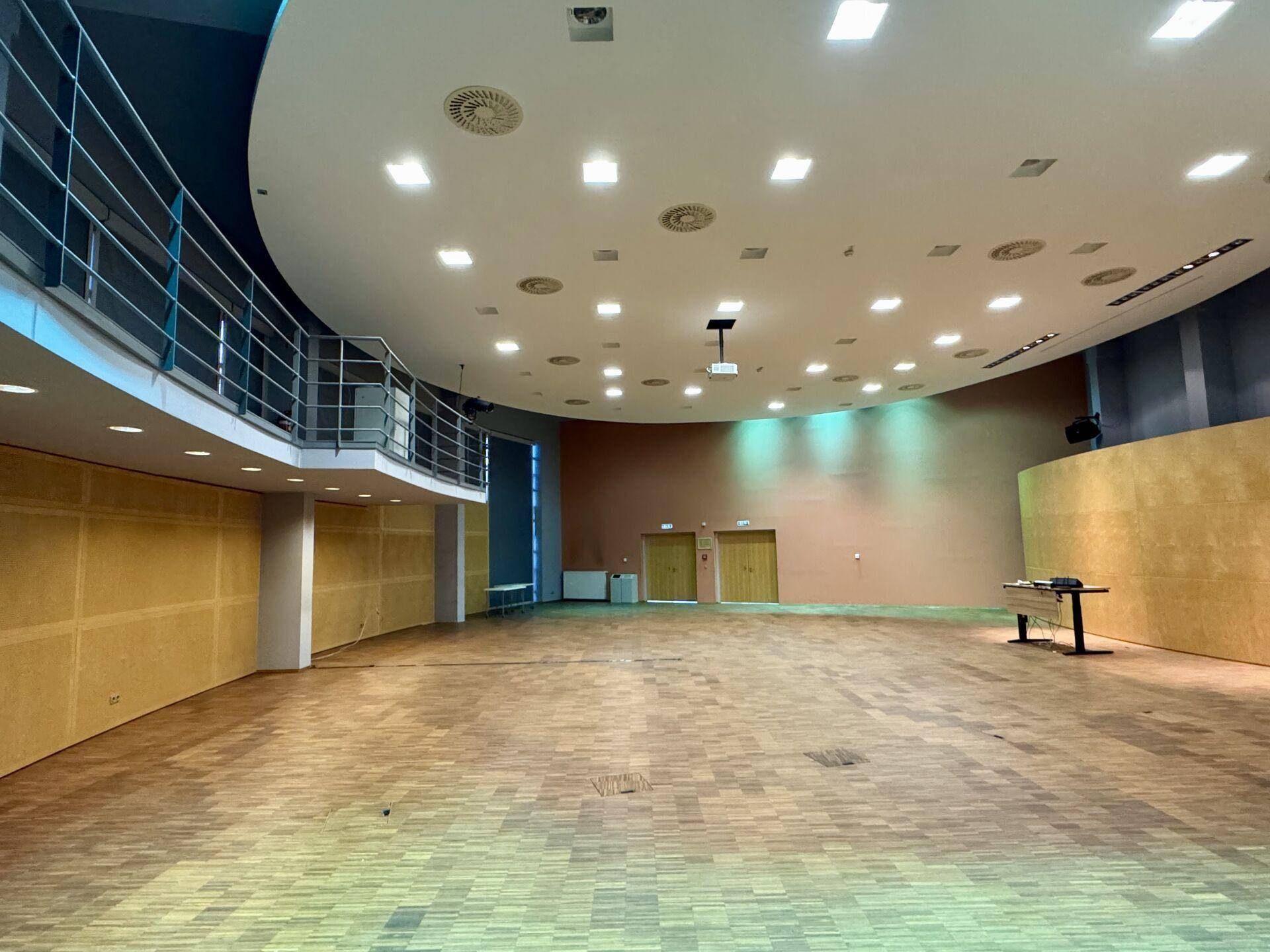 Großer, leerer Veranstaltungssaal mit Holzboden, runder Decke und einer Empore.