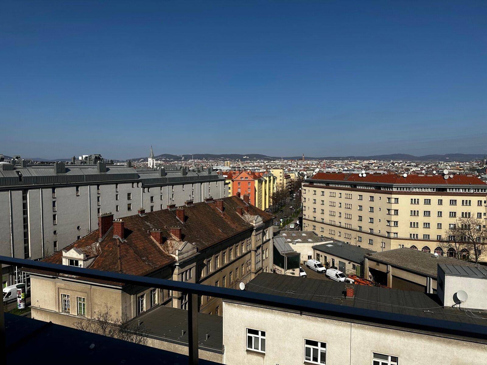 Weitläufiger Stadtblick von einem Balkon oder einer Terrasse mit vielen Gebäuden unter blauem Himmel.