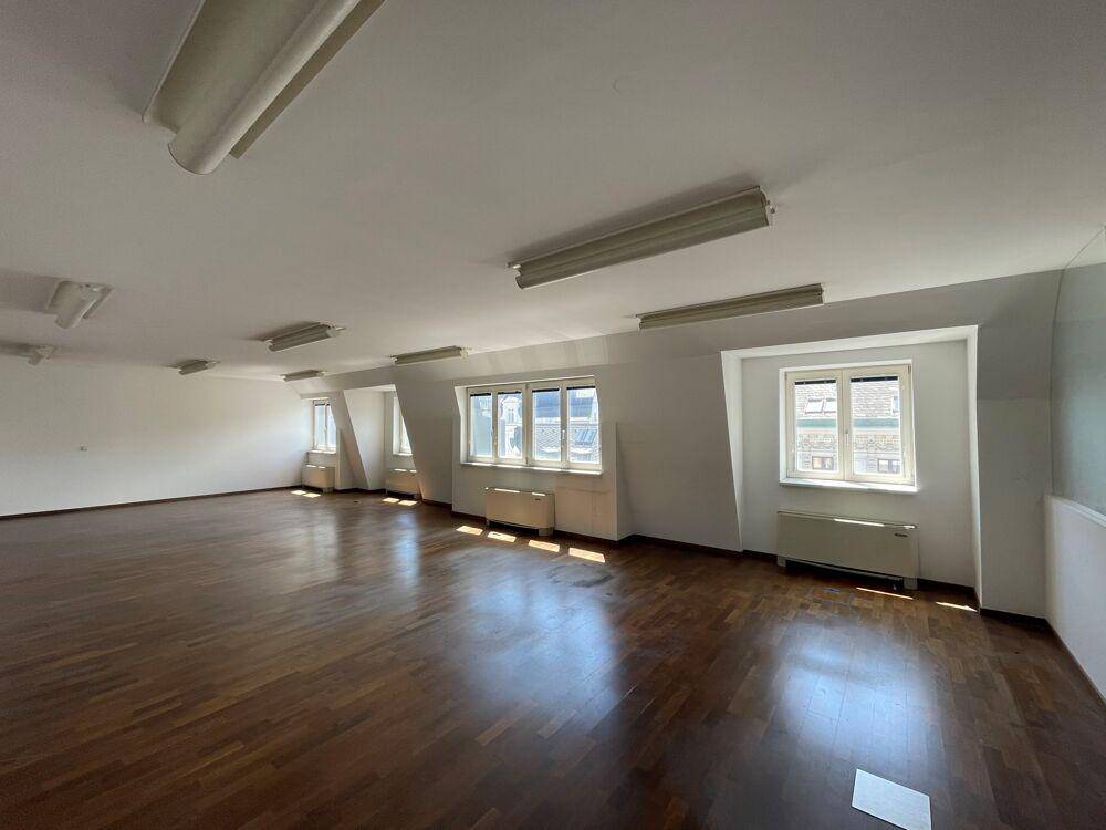 Großer, heller Raum mit Holzboden, vielen Fenstern und schrägen Wänden, ideal für Büronutzung.