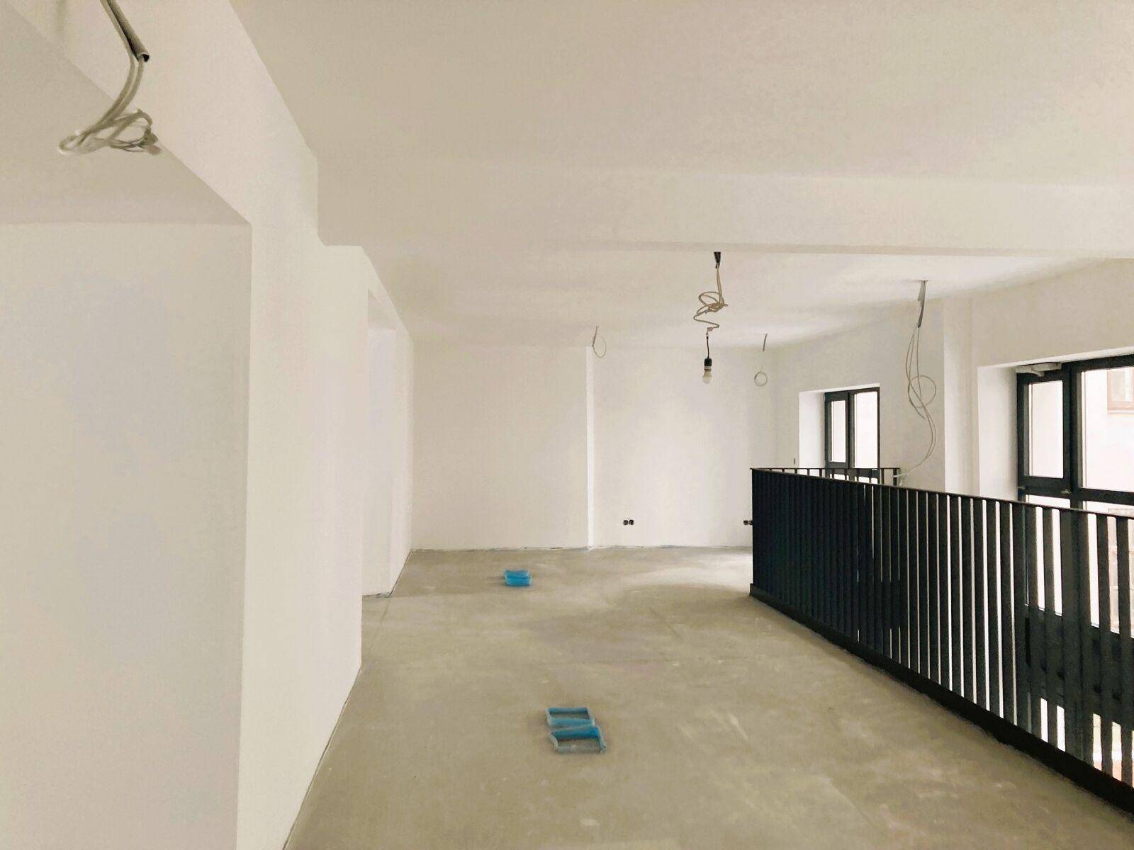 Geräumiger, heller Innenraum im Rohbau mit schwarzem Geländer einer Galerie und Betonboden.