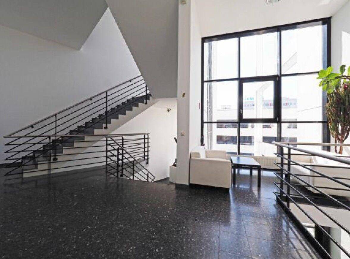 Heller Eingangsbereich mit großer Fensterfront, dunklem Terrazzoboden und moderner Treppe.