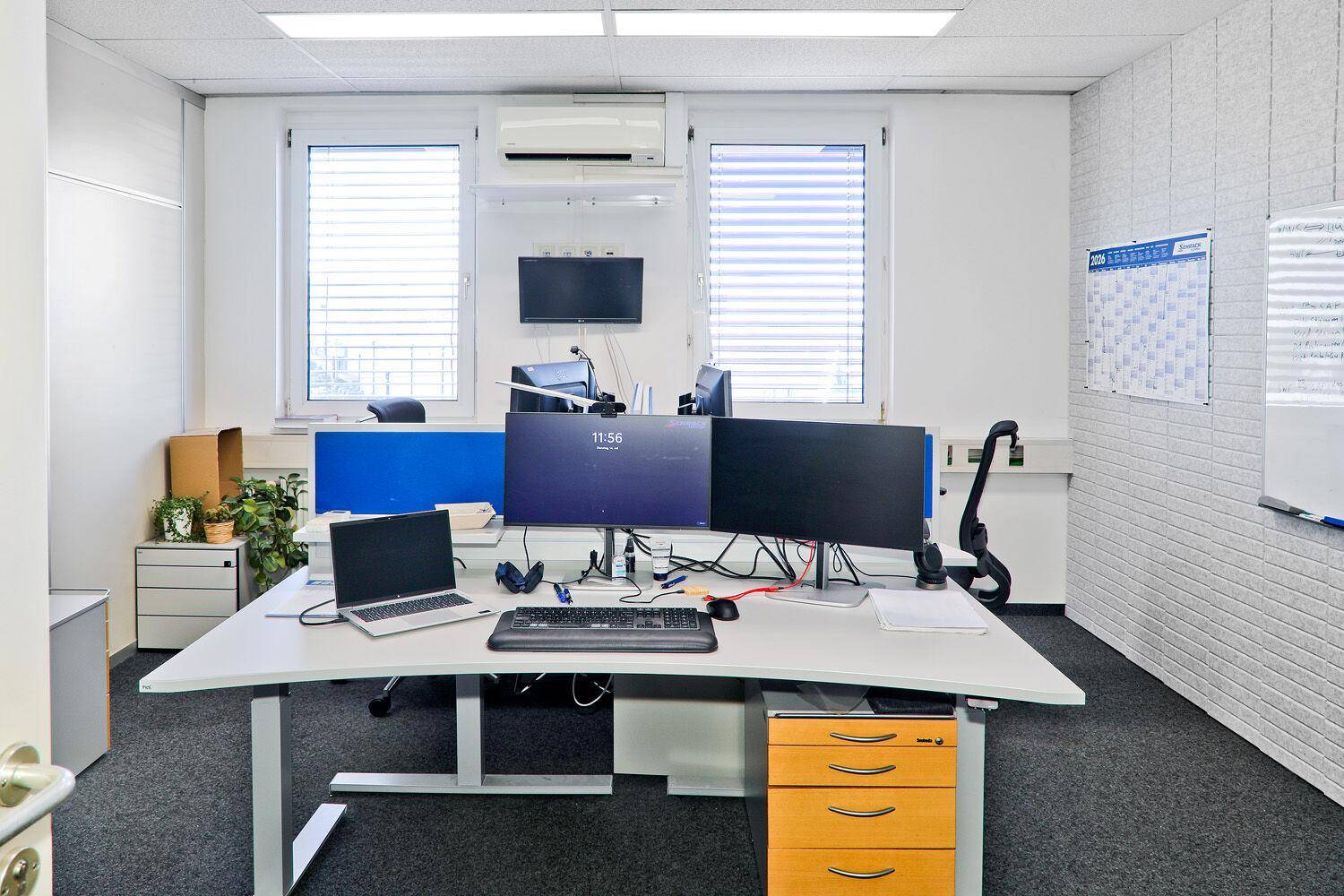 Einzelbüro mit zwei Arbeitsplätzen, Fenstern mit Jalousien und Klimaanlage.
