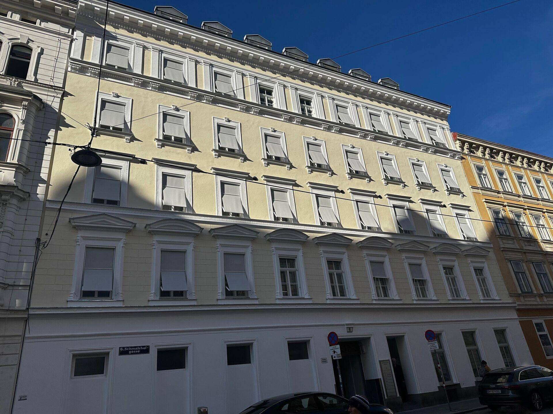 Ansicht der Gebäudefassade von der Straße mit geparkten Autos und Eingangsbereich.